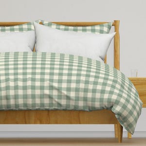 May include: A bed with a wooden frame and a green and white gingham patterned duvet cover. Two white pillows are on the bed. The bed is next to a wooden nightstand.