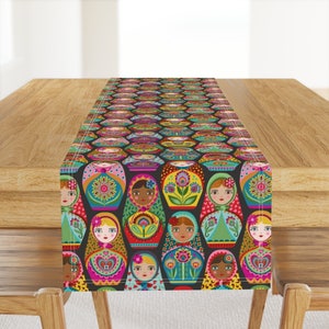 May include: A colorful table runner with a repeating pattern of Russian nesting dolls. The dolls are all different colors and have intricate designs. The background is black.