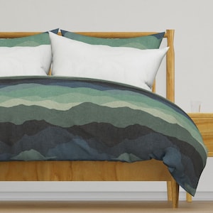 Puede incluir: Una funda nórdica con un patrón de cordillera en tonos azules y verdes. La funda nórdica está sobre un marco de cama de madera.
