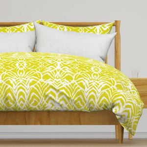 May include: A yellow and white patterned duvet cover on a wooden bed frame. The duvet cover has a geometric pattern with a white background and yellow lines.