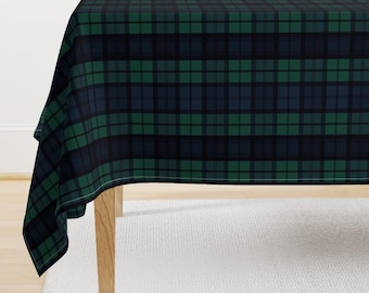 May include: A green and black plaid tablecloth with a white border. The tablecloth is draped over a wooden table.