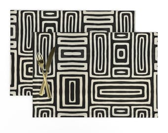 Könnte beinhalten: Zwei rechteckige Tischsets mit einem schwarz-weißen geometrischen Muster. Das Design zeigt eine Reihe von verbundenen Rechtecken und Quadraten. Eine goldene Gabel und ein Messer liegen auf einem der Tischsets.