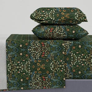 May include: A bedding set featuring a dark green floral pattern. The set includes two pillows stacked on top of a folded sheet. The pattern includes white, red, yellow, and blue floral elements. The bedding is likely made of a soft fabric.