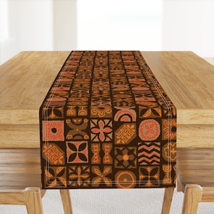 May include: A brown table runner with a geometric pattern in shades of orange and brown. The pattern is made up of squares and circles with various designs.