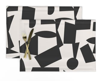 Könnte beinhalten: Ein Set mit zwei Platzsets mit geometrischem Muster in Schwarz und Weiß. Die Platzsets haben ein modernes, abstraktes Design auf cremefarbenem Hintergrund.