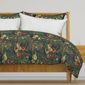 May include: A dark green duvet cover with a whimsical forest scene featuring dancing figures, foxes, and trees. The duvet cover is on a wooden bed frame with white pillows.
