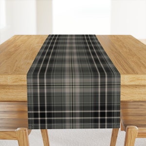 May include: A black and white plaid table runner with a subtle gray and cream pattern. The runner is on a wooden table.