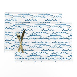 May include: Two blue and white watercolor wave patterned placemats with gold silverware on top.