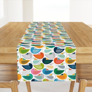 May include: A white table runner with a repeating pattern of colorful stylized birds. The birds are in shades of blue, green, yellow, orange, pink, and gray.