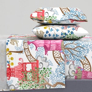 May include: Two rectangular pillows stacked on a bed runner, all featuring a white fabric base with a repeating pattern of pink pagodas, brown lattice arches, blue floral trees, grey clouds, and small spotted leopards in various poses.