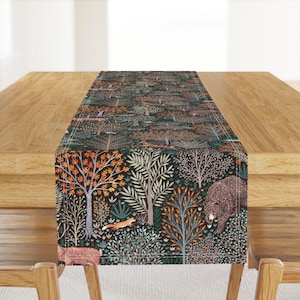 Könnte beinhalten: Ein rechteckiger Tischläufer mit einem dunklen Waldmuster auf schwarzem Grund. Das Design zeigt verschiedene Bäume mit orangefarbenen, grünen und weißen Blättern, durchsetzt mit Illustrationen eines Braunbären, eines Fuchses und eines Hirsches.