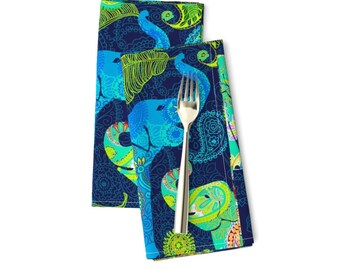 May include: Two blue and green patterned fabric napkins with a silver fork on top. The napkins feature a repeating pattern of elephants and paisley designs.