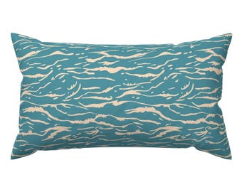 Puede incluir: Un cojín rectangular con fondo turquesa y un patrón de olas crema. El diseño presenta líneas curvas y fluidas que crean un efecto acuático. El cojín es un artículo decorativo, adecuado para una cama o sofá. Medidas en centímetros.