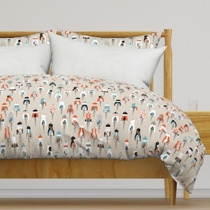 Puede incluir: Una funda nórdica y dos fundas de almohada con un patrón repetitivo de ciclistas en bicicletas en tonos naranja, azul verdoso, negro y blanco sobre un fondo beige claro, exhibidas en una estructura de cama de madera con cabecero.