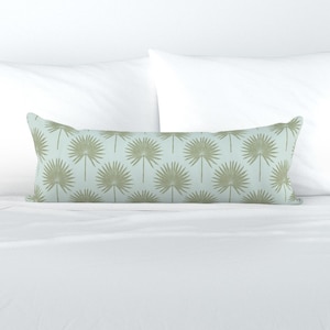 Puede incluir: Una almohada lumbar de color azul claro y verde con un diseño repetitivo de hojas de palma. La almohada está sobre una cama blanca.