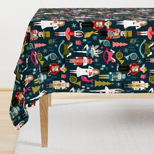 May include: A dark blue tablecloth featuring a repeating pattern of nutcrackers, ballerinas, rocking horses, French horns, and Christmas trees in shades of red, white, yellow, and green, interspersed with small white snowflake icons.