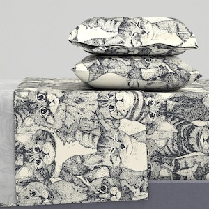May include: A white and black patterned bedding set with a repeating pattern of cats' faces. The bedding set includes a fitted sheet, flat sheet, and two pillowcases.