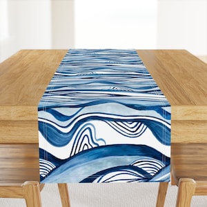 May include: A blue and white table runner with a wavy abstract pattern. The runner is made of fabric and has a white background with blue waves and lines.