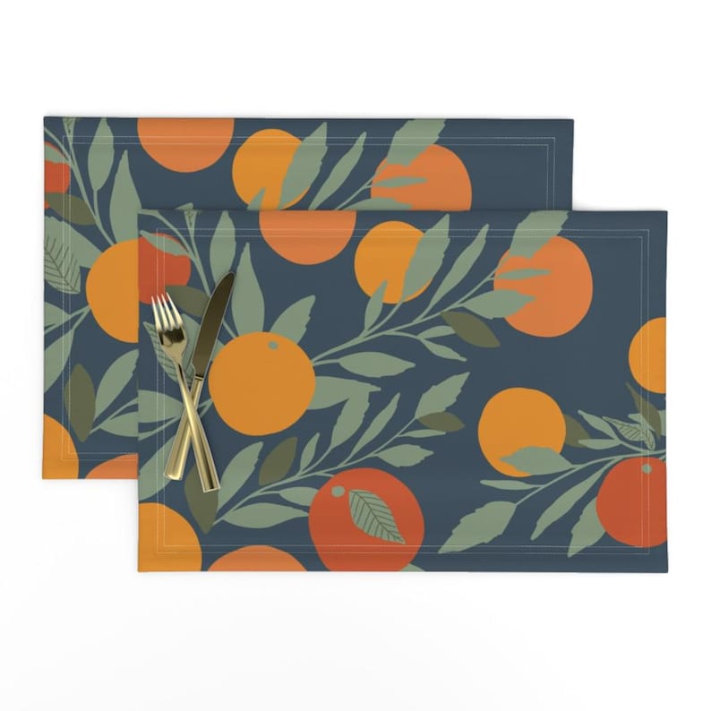 May include: Two blue placemats with a repeating pattern of orange and red oranges with green leaves. The placemats are made of fabric and have a subtle texture.