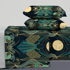 Puede incluir: Un juego de cama azul oscuro y verde con un patrón geométrico que presenta detalles dorados y lunas estilizadas. El juego incluye una sábana plana, una sábana ajustable y dos fundas de almohada.