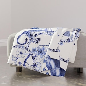 May include: A white throw blanket with a blue and white pattern of a leopard, monkey, and flowers. The pattern is reminiscent of blue and white china.