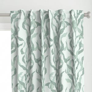 Op de afbeelding: Een paar lichtgroene gordijnen met een witte achtergrond en een herhalend patroon van gestileerde zeewier.