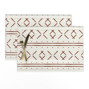 May include: Two white placemats with a geometric pattern in a rust brown color. The pattern is a series of diamonds and lines.