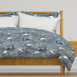 Puede incluir: Una funda nórdica azul y blanca con un patrón de olas y un monstruo marino. La funda nórdica está sobre un marco de cama de madera.