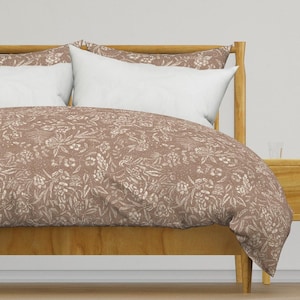 May include: A brown duvet cover with a white floral pattern. The duvet cover is on a bed with a wooden headboard and two white pillows.