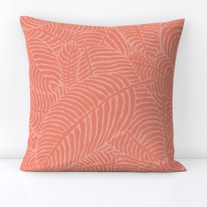 May include: A coral-colored throw pillow with a pattern of stylized leaves. The leaves are outlined in a darker shade of coral and have a textured appearance.