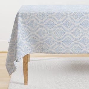 May include: A white tablecloth with a blue floral pattern. The tablecloth has a wavy design with a repeating pattern of small blue flowers and leaves.