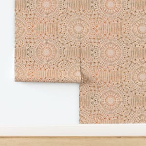 May include: Wallpaper roll featuring a repeating pattern of circular designs in shades of beige, orange, and brown. The design includes radiating lines and geometric shapes, creating a textured appearance. The wallpaper is partially unrolled, revealing the pattern.