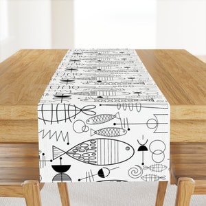 Puede incluir: Un camino de mesa blanco y negro con un patrón geométrico de peces estilizados y formas abstractas. El camino de mesa está sobre una mesa de madera.