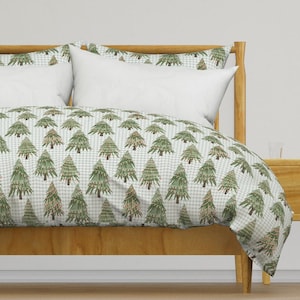May include: A white and green duvet cover with a repeating pattern of stylised Christmas trees. The duvet cover is on a wooden bed frame with a white headboard.