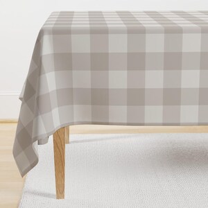 May include: A beige and white checkered tablecloth with a simple design. The tablecloth is draped over a table with wooden legs.