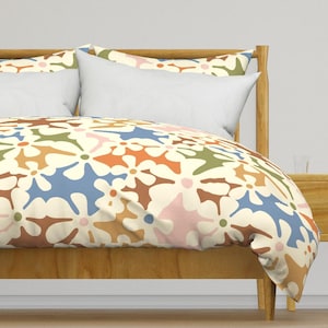 May include: A white duvet cover with a floral pattern in shades of brown, orange, blue, and pink. The duvet cover is on a wooden bed frame.