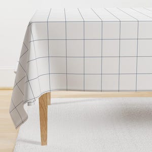 May include: White tablecloth with a grid pattern in navy blue. The tablecloth is draped over a wooden table with a white rug underneath.