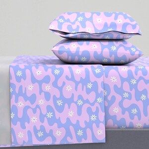 Puede incluir: Un juego de ropa de cama con un patrón abstracto azul claro y rosa con flores blancas. La ropa de cama incluye una sábana bajera, una sábana plana y dos fundas de almohada.