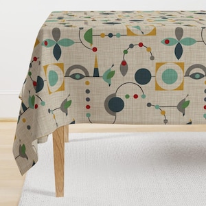 May include: Beige tablecloth featuring a repeating geometric pattern in teal, yellow, grey, and red. The design includes abstract shapes, such as circles, squares, and floral-like elements, connected by thin black lines. The tablecloth is draped over a wooden table.
