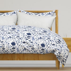 May include: A white duvet cover featuring a blue and white pattern of sea creatures, such as fish, jellyfish, and crabs. The duvet cover is on a wooden bed frame with a white pillow.