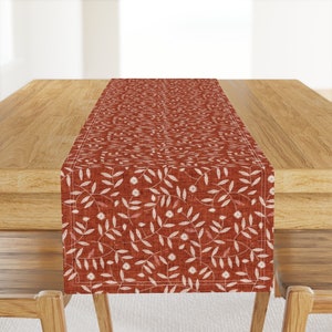 May include: A red table runner with a white floral pattern. The runner is made of a linen-like fabric and has a subtle texture.
