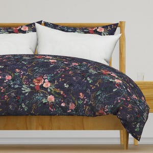 May include: A dark blue duvet cover with a floral pattern featuring pink, red, and white flowers. The duvet cover is on a wooden bed frame.