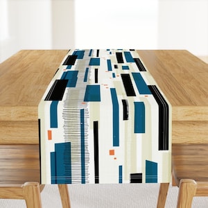 May include: A geometric table runner with a white background and blue, black, and orange stripes. The runner has a modern, abstract design.