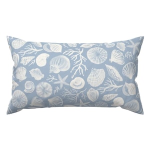May include: A rectangular pillow with a light blue background and a white seashell pattern. The design includes various seashells, starfish, and coral branches, creating a coastal theme. The pillow is a decorative item for a bed or sofa.