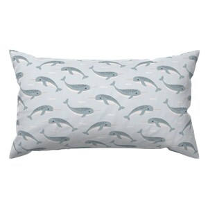 May include: A light blue rectangular pillow with a repeating pattern of narwhals swimming in a light blue sea. The narwhals are a light blue color with a white horn and a black eye.