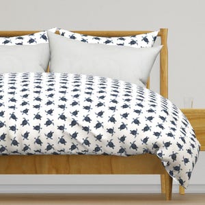 May include: A white duvet cover with a navy blue sea turtle pattern. The duvet cover is on a bed with a wooden headboard and a white pillow.