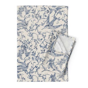 May include: A blue and white tea towel with a floral and bird pattern. The design features delicate branches with small flowers and birds in flight.