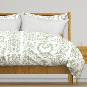 May include: A white duvet cover with a green floral pattern. The duvet cover is on a bed with a wooden headboard and two white pillows.
