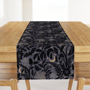 May include: A black and gold table runner with a spooky forest design. The pattern features bats, mushrooms, crescent moons, and stars on a dark gray background.
