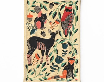 Op de afbeelding: Een beige keukendoek met een kleurrijk patroon van een hert, eekhoorn, uil en vos. De dieren zijn gestileerd en hebben geometrische patronen. De achtergrond is crèmekleurig met groene bladeren en bloemen.